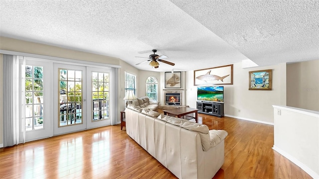 living area with a textured ceiling, ceiling fan, wood finished floors, baseboards, and a glass covered fireplace