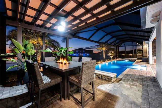 pool at dusk with a patio, pool water feature, and a lanai