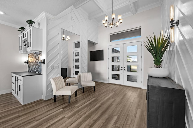 living area featuring french doors, coffered ceiling, an inviting chandelier, crown molding, and dark hardwood / wood-style flooring