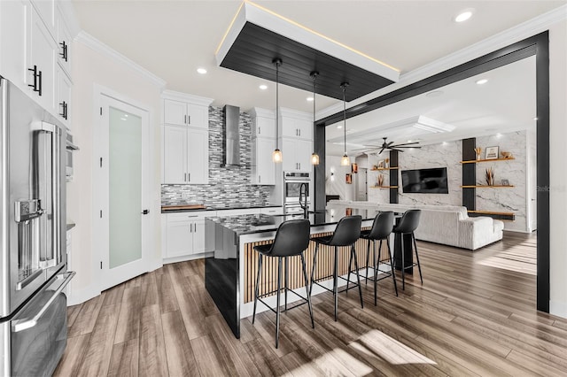 kitchen featuring white cabinetry, an island with sink, pendant lighting, stainless steel appliances, and wall chimney range hood