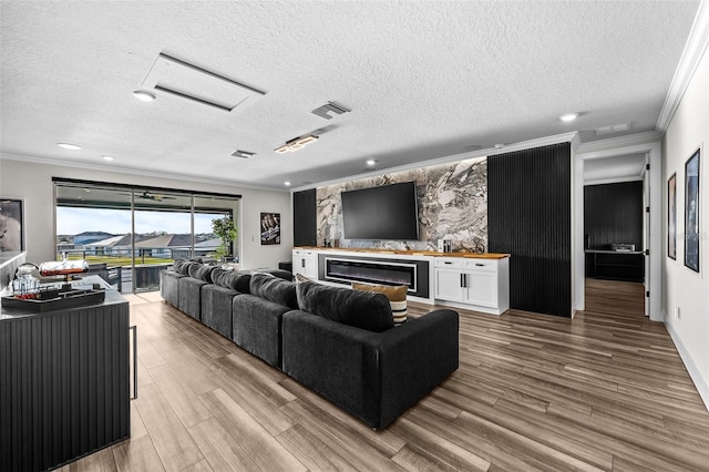 living room featuring crown molding, a fireplace, a textured ceiling, and light wood-type flooring