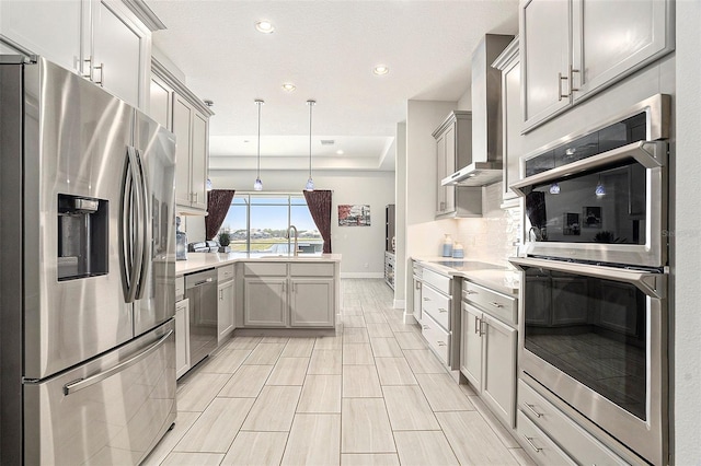 kitchen with a peninsula, a sink, appliances with stainless steel finishes, wall chimney range hood, and backsplash