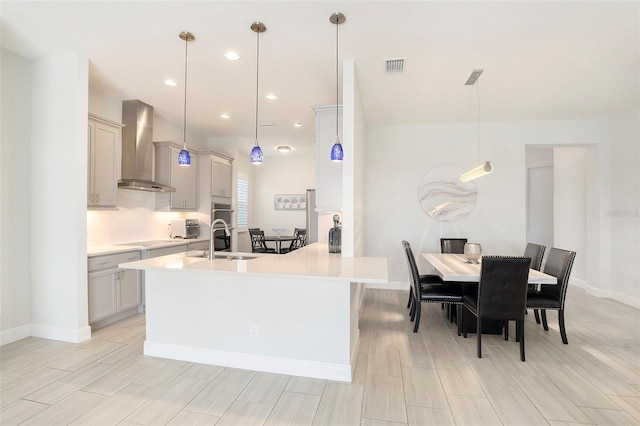 kitchen with visible vents, stovetop, a sink, light countertops, and wall chimney exhaust hood