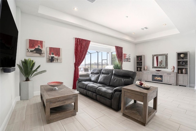 living room with baseboards, a raised ceiling, visible vents, and a fireplace