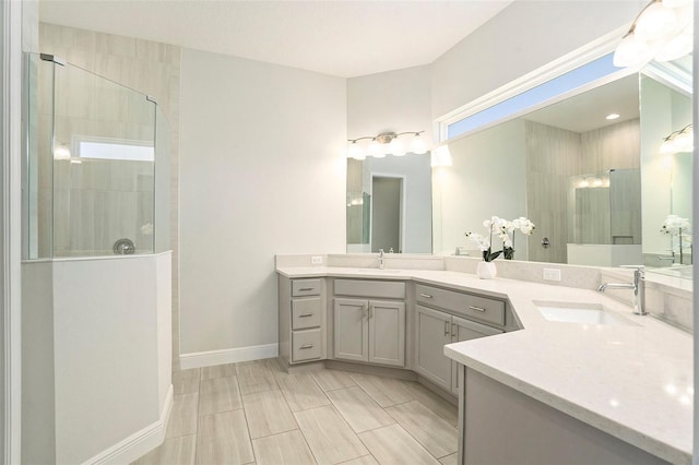 full bath featuring double vanity, tiled shower, baseboards, and a sink