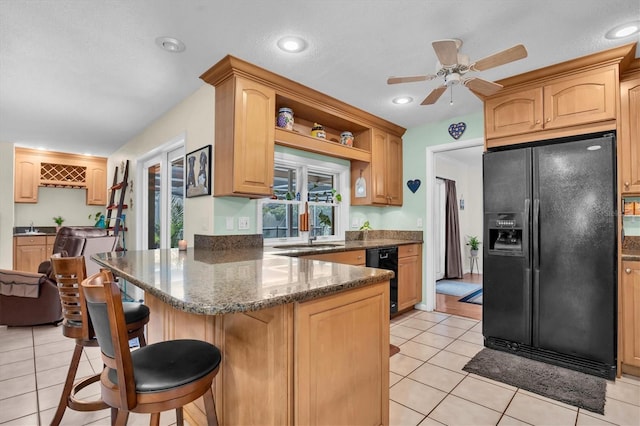 kitchen with light tile patterned floors, a breakfast bar area, black appliances, dark stone counters, and light brown cabinets