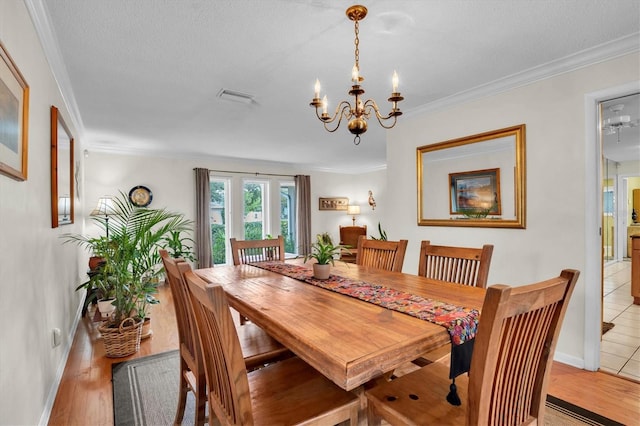 dining space with ornamental molding, a textured ceiling, an inviting chandelier, and light hardwood / wood-style flooring