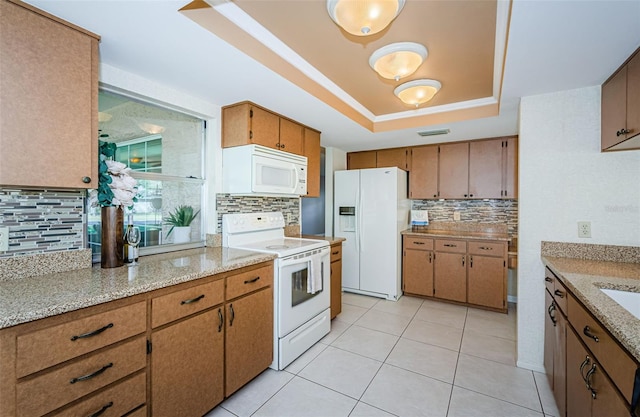 kitchen with a raised ceiling, light tile patterned flooring, backsplash, and white appliances