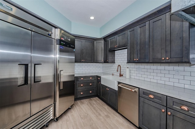 kitchen with sink, decorative backsplash, light wood-type flooring, and appliances with stainless steel finishes