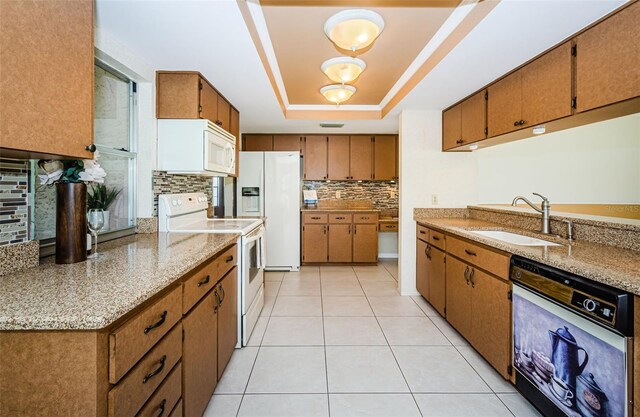 kitchen featuring sink, light tile patterned floors, a raised ceiling, white appliances, and light stone countertops