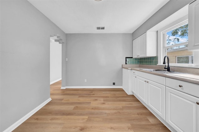 kitchen featuring sink, backsplash, white cabinets, and light hardwood / wood-style floors