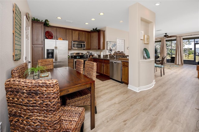 kitchen with ceiling fan, stainless steel appliances, dark stone counters, and light wood-type flooring