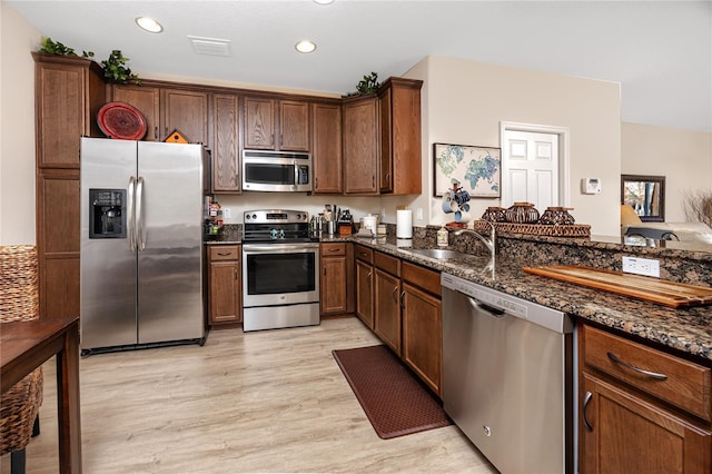 kitchen featuring dark stone countertops, sink, light hardwood / wood-style floors, and appliances with stainless steel finishes