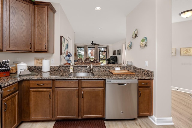 kitchen featuring sink, dishwasher, kitchen peninsula, dark stone counters, and light wood-type flooring