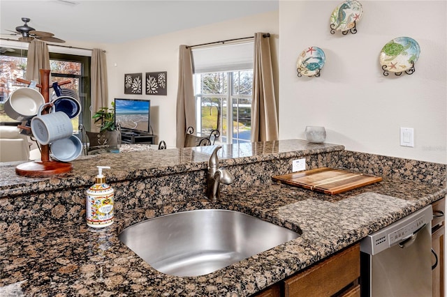 kitchen with sink, stainless steel dishwasher, dark stone counters, and ceiling fan