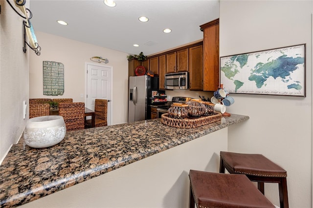 kitchen featuring dark stone countertops, a breakfast bar, kitchen peninsula, and appliances with stainless steel finishes