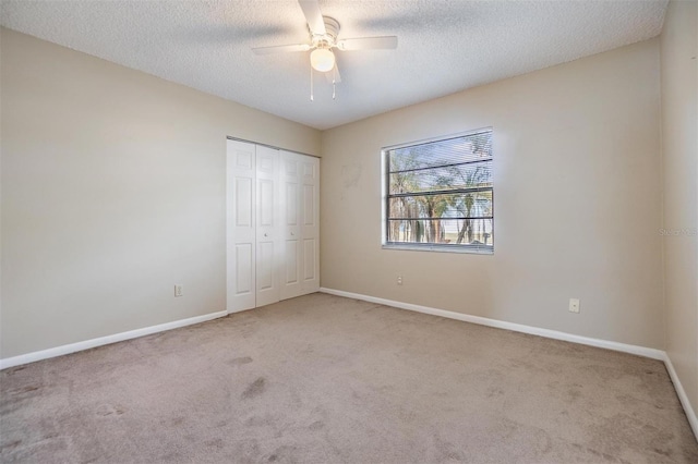 unfurnished bedroom with ceiling fan, light carpet, a closet, and a textured ceiling