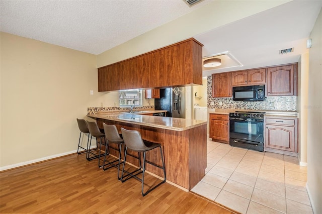 kitchen featuring a breakfast bar, tasteful backsplash, light hardwood / wood-style floors, black appliances, and kitchen peninsula