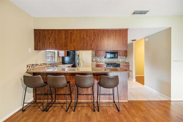 kitchen featuring decorative backsplash, kitchen peninsula, a textured ceiling, and range