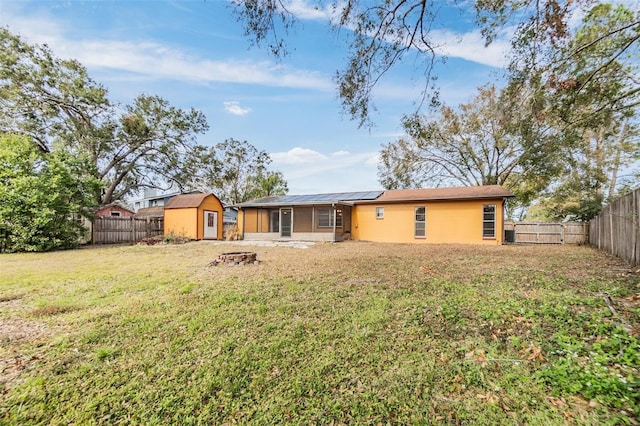 rear view of property with a storage shed, a yard, and solar panels