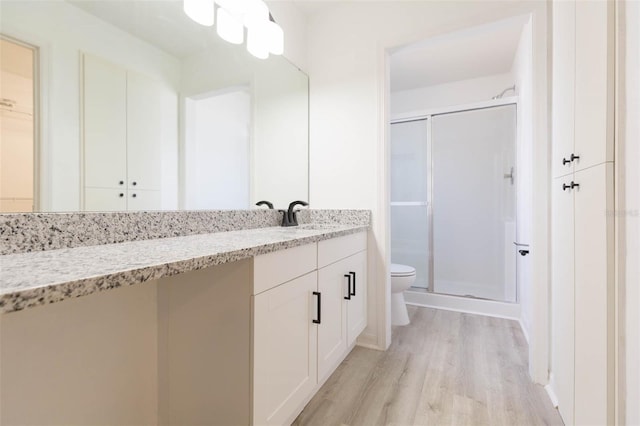 bathroom with wood-type flooring, toilet, a shower with shower door, and vanity