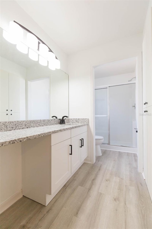 bathroom featuring hardwood / wood-style flooring, vanity, toilet, and a shower with shower door