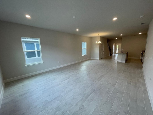 unfurnished living room featuring an inviting chandelier and light hardwood / wood-style floors