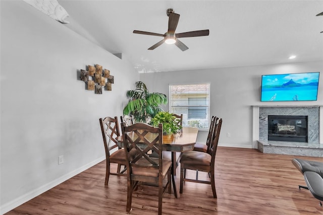 dining space featuring wood-type flooring, vaulted ceiling, ceiling fan, and a fireplace