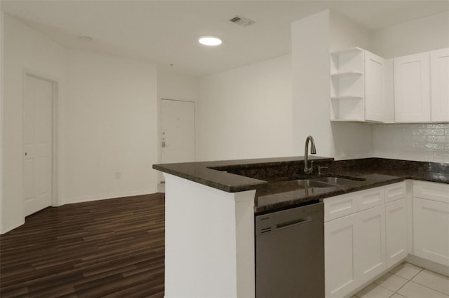 kitchen featuring kitchen peninsula, stainless steel dishwasher, dark stone counters, and white cabinets