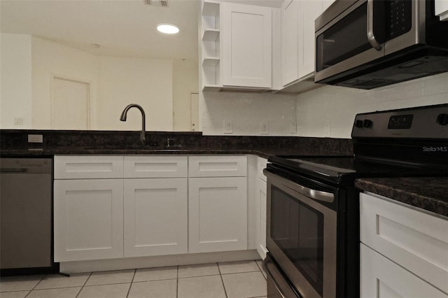 kitchen featuring white cabinetry, sink, dark stone counters, light tile patterned floors, and stainless steel appliances