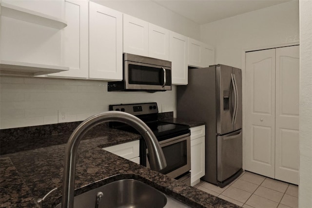 kitchen with light tile patterned floors, sink, white cabinetry, dark stone countertops, and stainless steel appliances