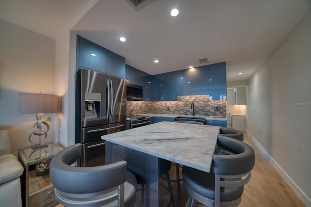 kitchen featuring sink, light hardwood / wood-style flooring, blue cabinetry, stainless steel appliances, and decorative backsplash