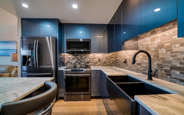 kitchen featuring blue cabinetry, sink, tasteful backsplash, light hardwood / wood-style flooring, and appliances with stainless steel finishes