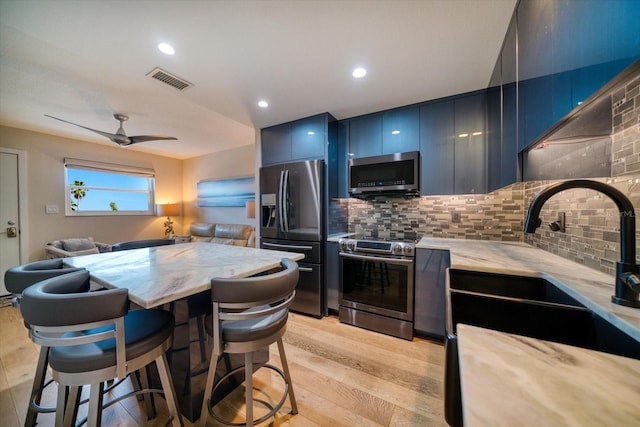 kitchen with sink, a breakfast bar, stainless steel appliances, blue cabinets, and decorative backsplash