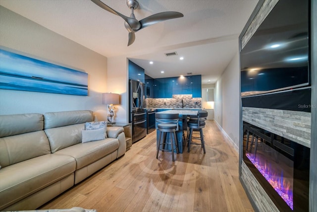 living room with ceiling fan, a fireplace, sink, and light wood-type flooring