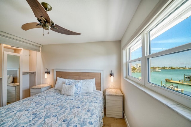 bedroom with a water view, hardwood / wood-style floors, and ceiling fan