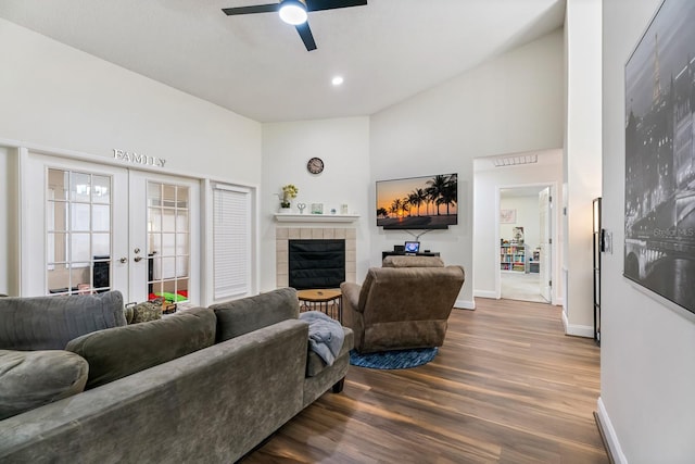 living room with hardwood / wood-style floors, high vaulted ceiling, a tiled fireplace, ceiling fan, and french doors