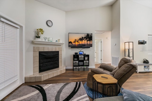 living room featuring a tiled fireplace, dark hardwood / wood-style floors, and a towering ceiling