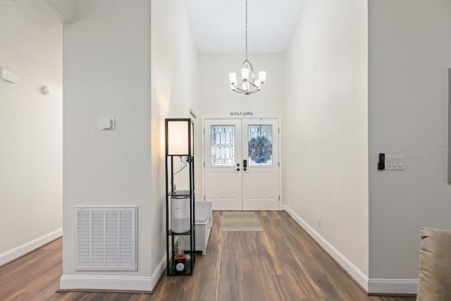 entrance foyer with french doors, a towering ceiling, dark hardwood / wood-style flooring, and a chandelier