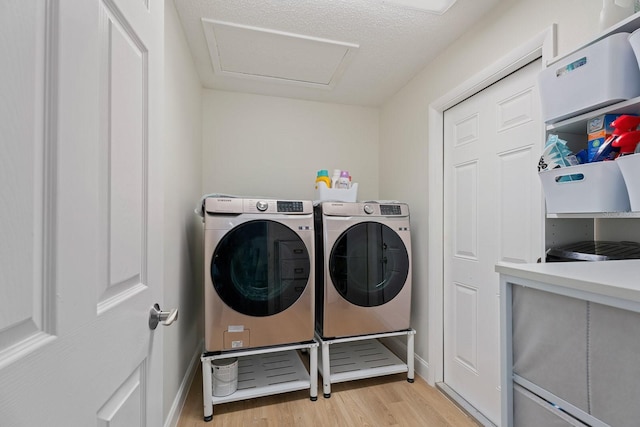 clothes washing area with separate washer and dryer, a textured ceiling, and light wood-type flooring