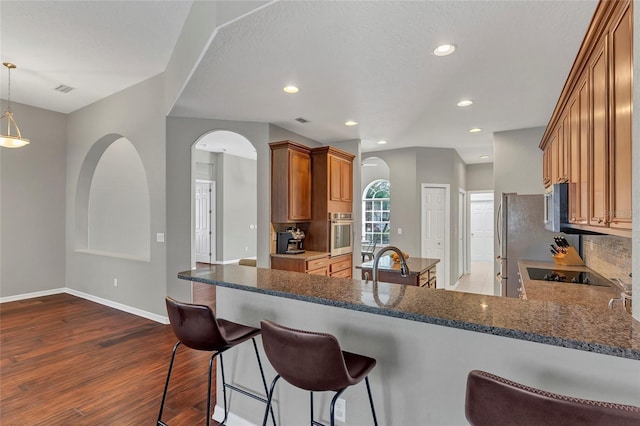 kitchen with dark wood-type flooring, hanging light fixtures, stainless steel appliances, decorative backsplash, and kitchen peninsula