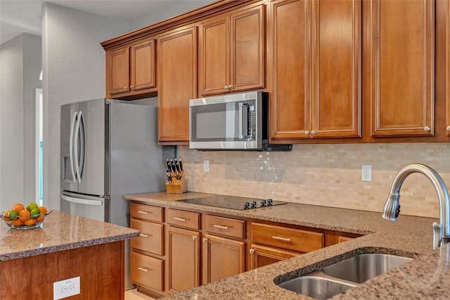 kitchen with stainless steel appliances, light stone countertops, sink, and backsplash