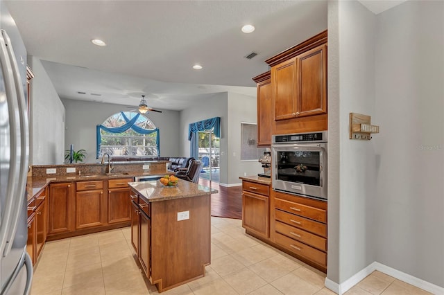 kitchen featuring light tile patterned flooring, appliances with stainless steel finishes, sink, a center island, and light stone counters