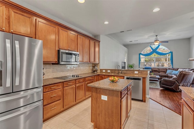 kitchen featuring sink, light stone counters, appliances with stainless steel finishes, kitchen peninsula, and a kitchen island