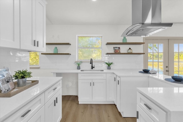 kitchen featuring sink, white cabinetry, light hardwood / wood-style flooring, island exhaust hood, and backsplash