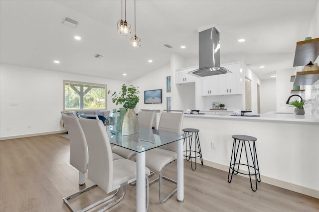 dining space featuring vaulted ceiling, sink, and light hardwood / wood-style floors