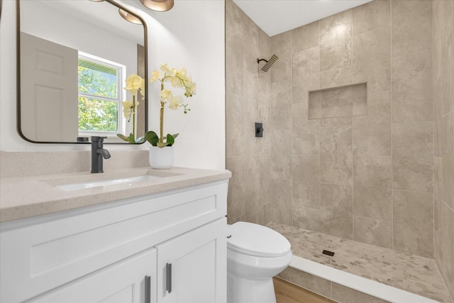 bathroom featuring hardwood / wood-style flooring, vanity, tiled shower, and toilet