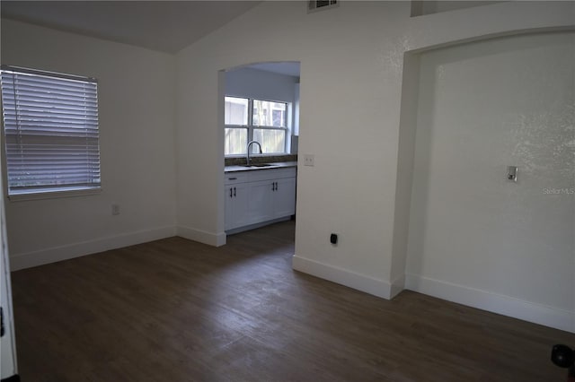 unfurnished room featuring visible vents, dark wood-type flooring, baseboards, lofted ceiling, and a sink