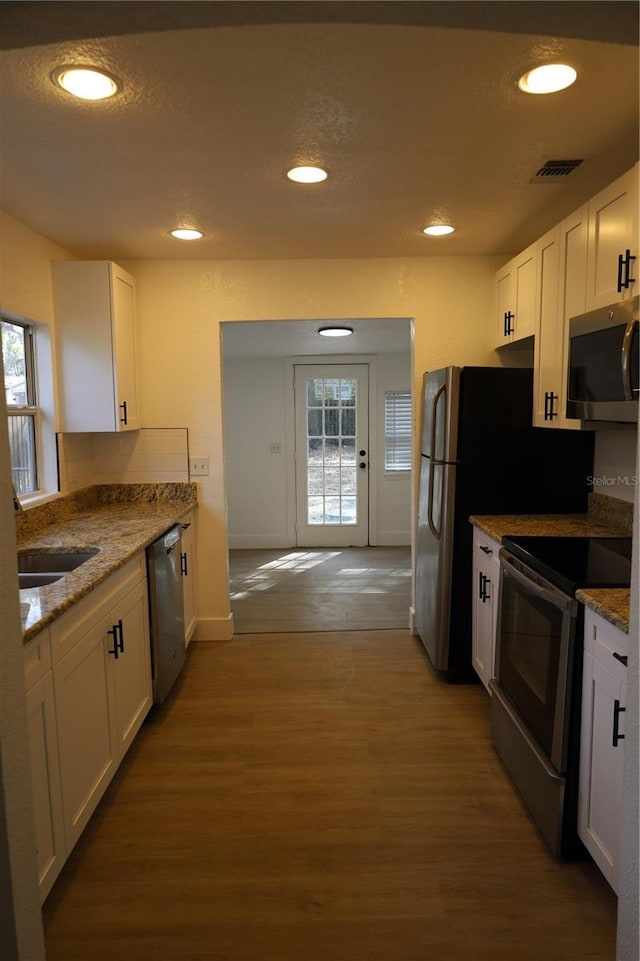 kitchen with a wealth of natural light, white cabinetry, stainless steel appliances, and wood finished floors