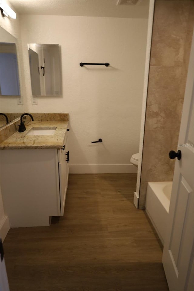 bathroom featuring baseboards, toilet, a bathing tub, wood finished floors, and vanity